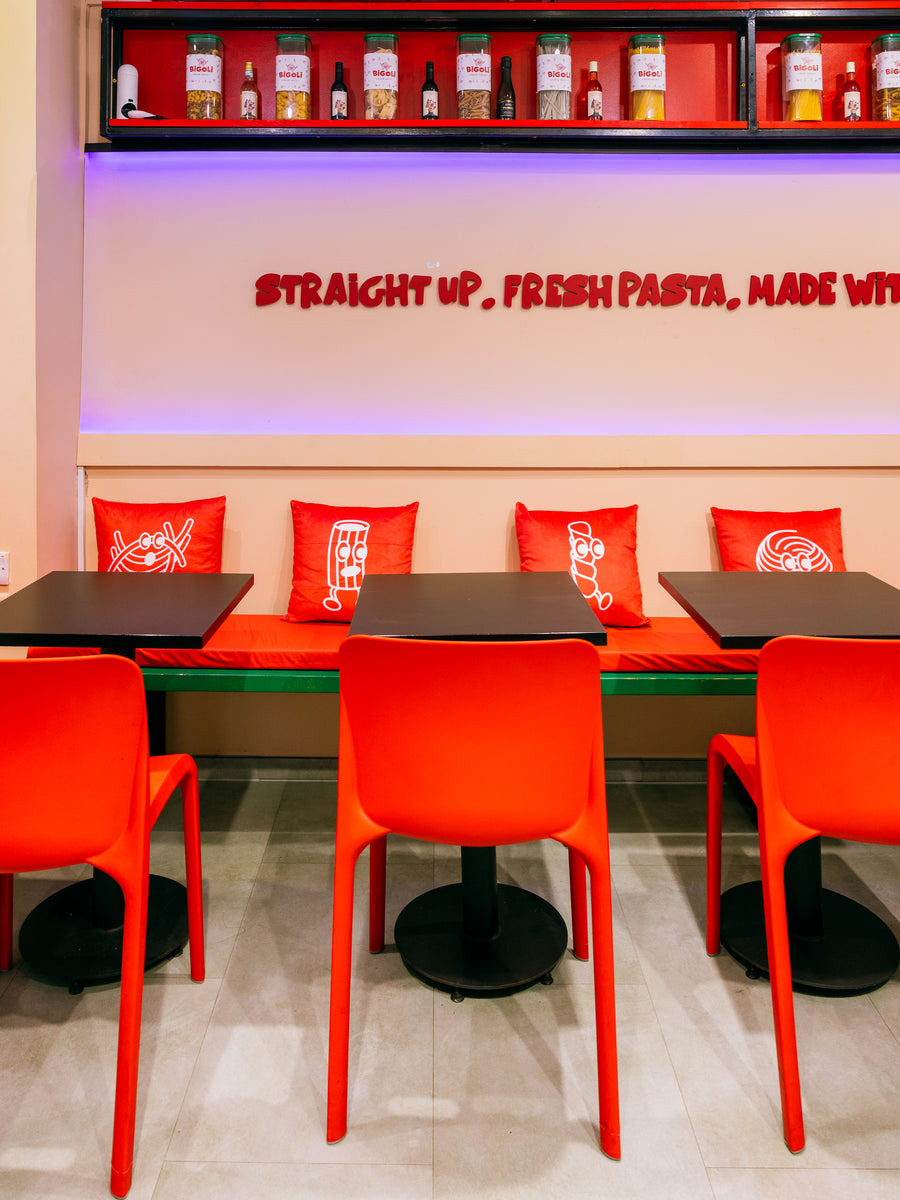 Red stools and tables inside Bigoli in Old Street, under the neon sign
