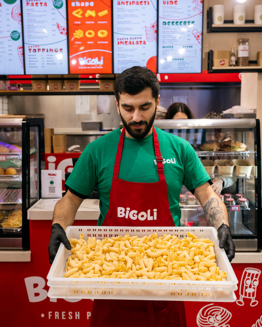 A Bigoli chef carrying a tray of fresh pasta past the menu screens.